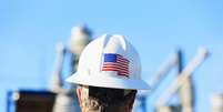 Homem com capacete de trabalho que tem bandeira dos EUA; ele observa planta industrial  Foto: Getty Images / BBC News Brasil