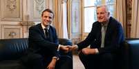 Macron (à esquerda) aperta a mão de Barnier, escolhido como o novo primeiro-ministro  Foto: Ludovic Marin/Pool/AFP / BBC News Brasil