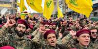 Integrantes do Hezbollah em uniformes militares marcham com bandeiras do grupo ao fundo.  Foto: Getty Images / BBC News Brasil