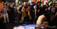 Iraniano pisa em bandeira de Israel durante comemoração em Teerã pelos ataques com mísseis nesta terça-feira (01/10)  Foto: Majid Asgaripour/WANA via REUTERS / BBC News Brasil