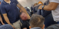 Homem é contido por passageiros após fazer aeromoça de refém e tentar abrir porta de avião  Foto: Reprodução