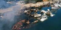 Um grande barco afundado perto do cais na cidade portuária síria de Latakia. Há fumaça subindo e estruturas metálicas parcialmente submersas.  Foto: Getty Images / BBC News Brasil