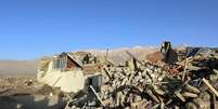 Pessoas em cima de uma casa desabada, ao lado de uma pilha de escombros. Ao fundo, montanhas.  Foto: Reuters / BBC News Brasil