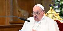 O Papa Francisco sentado em uma cadeira de veludo, lendo de uma folha de papel. Ele está falando em um microfone. O fundo está desfocado  Foto: Getty Images / BBC News Brasil