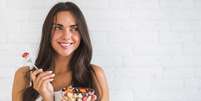 Mulher comendo salada de frutas  Foto: Freepik