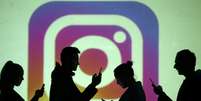 Pessoas utilizando o celular diante da logo do Instagram  Foto: Dado Ruvic / Reuters