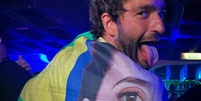 Humberto Carrão se enrola em bandeira com rosto de Fernanda Torres  Foto: Reprodução/Instagram