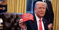 Trump no Salão Oval da Casa Branca segurando boné vermelho com a estampa "Trump estava certo sobre tudo" em inglês  Foto: Getty Images / BBC News Brasil