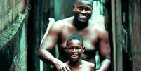 Pai e filho são fotografados em viela  Foto: Reprodução do Livro Favela Arte e Poesia / Flipar
