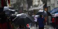 Pedestres se protegem da chuva, com termômetros marcando 23ºC graus, na região central da capital paulista, na tarde desta sexta-feira, 04 de abril de 2025.  Foto: CRIS FAGA/DRAGONFLY PRESS/ESTADÃO CONTEÚDO