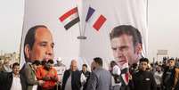Egípcios caminham em frente a um banner de apoio ao presidente egípcio Abdel-Fattah el-Sissi, à esquerda, e seu homólogo francês Emmanuel Macron, durante a visita deles à cidade de Arish, no norte da Península do Sinai, cerca de 50 km (32 milhas) a oeste da fronteira com a Faixa de Gaza, Egito, terça-feira, 8 de abril de 2025. (Foto/AP/Mohamed Arafat)  Foto: AP - Mohammed Arafat / RFI