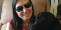 Danieli Haloten sentada com a labradora preta Elva, sua cão-guia aposentada, em seu colo em uma foto publicada no Instagram  Foto: Reprodução/Instagram / Contigo