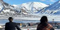Noruegueses andando de bicicleta em Svalbard, com picos cobertos de neve ao fundo  Foto: BBC News Brasil