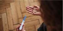Mulher segura aparelho de teste de gravidez com uma m&atilde;o e p&iacute;lula na outra, olhando para o ch&atilde;o  Foto: Getty Images / BBC News Brasil