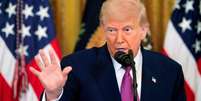 Donald Trump de terno com a mão levantada, em frente a bandeiras dos EUA  Foto: Getty Images / BBC News Brasil