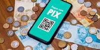 Celular com tela mostrando Pix e notas e moedas de real ao fundo  Foto: Getty Images / BBC News Brasil