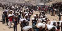 Palestinos caminham com sacos de farinha depois que caminhões carregados de ajuda humanitária entraram no norte de Gaza, em 27 de julho de 2025.  Foto: © BASHAR TALEB / AFP / RFI