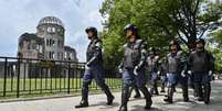 Policiais em equipamento anti-motim marcham em frente ao Domo da Bomba Atômica (ao fundo, à esquerda) enquanto protegem a área um dia antes das cerimônias que marcam o 80º aniversário do primeiro bombardeio atômico do mundo, na cidade de Hiroshima, província de Hiroshima, em 5 de agosto de 2025.  Foto: AFP - RICHARD A. BROOKS / RFI