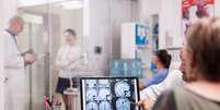 Senior woman in hospital office looking at brain ct  Foto: scan while discussing with doctor about diagnosis. Sick young woman and elderly medic with grey hair in clinic corridor. / Revista Malu