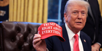 O presidente Donald Trump segura um chapéu e afirma: "Trump estava certo sobre tudo" após assinar decretos no Salão Oval da Casa Branca  Foto: Alex Wong/Getty Images