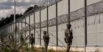Soldados de fronteira armados montam guarda frente a uma alta e longa barreira metálica com concertinas de arame farpado  Foto: Getty Images / BBC News Brasil