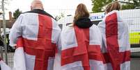 Três pessoas de costas envoltas na bandeira da Inglaterra  Foto: PA Media / BBC News Brasil