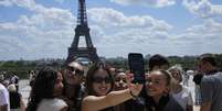 Turistas posam para uma selfie com a Torre Eiffel ao fundo em 6 de julho de 2023, em Paris (imagem ilustrativa).  Foto: AP - Michel Euler / RFI
