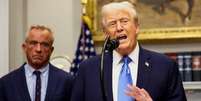 Donald Trump fala de uma tribuna durante uma entrevista coletiva na Casa Branca, acompanhado por Robert F. Kennedy Jr.   Foto: Reuters / BBC News Brasil