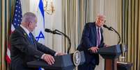 Netanyahu e Trump se olham, cada um de seu palanque em salão com bandeiras dos respectivos países  Foto: Reuters / BBC News Brasil