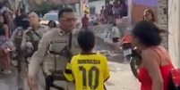 Um menino que não aparenta ter mais que 12 anos se coloca entre a mulher e o policial militar  Foto: Reprodução/X