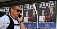 Homem passa diante de um cartaz com os presidentes Javier Milei e Donald Trump, em Buenos Aires, em 14 de outubro de 2025.  Foto: © Luis ROBAYO / AFP / RFI