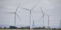 Turbinas eólicas terrestres no Parque Eólico Little Cheyne Court operam ao lado de torres de eletricidade em Dungeness, Grã-Bretanha, em 10 de julho de 2024. Ilustração.  Foto: © Chris J Ratcliffe / REUTERS / RFI