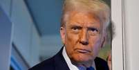 Donald Trump conversando com jornalistas a bordo do avião presidencial em 29 de outubro de 2025. Ele veste um paletó escuro, apoia uma das mãos na porta e olha para fora. Foto: Getty Images / BBC News Brasil