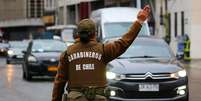 Uma policial chilena vista de costas vestindo uniforme marrom com colete a prova de balas onde se lê "Carabineros de Chile". Ela tem o braço direito erguido e faz sinal para veículos na rua desviarem  Foto: Getty Images / BBC News Brasil
