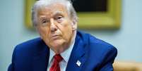 O presidente dos EUA, Donald Trump, sentado, com um terno azul, camisa azul, gravata vermelha e um broche na lapela com a bandeira do pa&iacute;s  Foto: EPA/Shutterstock / BBC News Brasil