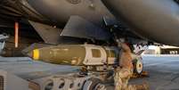 Um militar da For&ccedil;a A&eacute;rea dos Estados Unidos instala um sistema de muni&ccedil;&atilde;o GBU‑31 em um ca&ccedil;a F‑15E Strike Eagle em uma base do Comando Central americano (Centcom), em 19 de dezembro de 2025.  Foto: via REUTERS - U.S. Air Force / RFI