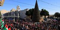 Cenenas de fi&eacute;is se re&uacute;nem ao lado da &aacute;rvore de Natal na Pra&ccedil;a da Manjedoura, na v&eacute;spera de Natal, na Cidade Velha de Bel&eacute;m, na Cisjord&acirc;nia ocupada por Israel, em 24 de dezembro de 2025.  Foto: REUTERS - Mussa Qawasma / RFI