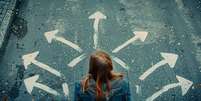 Choosing future profession. Girl standing in front of drawn signs on asphalt, top view. Arrows pointing in different directions as diversity of opportunities Foto: Revista Malu