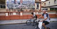 Moradores circulam de bicicleta nas ruas de Havana, em frente a um cartaz com imagens do presidente de Cuba, Miguel D&iacute;az-Canel (&agrave; dir.), e de seus antecessores no cargo, Fidel (&agrave; esq.) e Ra&uacute;l Castro, em 16 de fevereiro de 2026. Foto: &copy; Yamil Lage / AFP / RFI