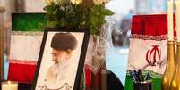 Retrato do líder supremo do Irã, o aiatolá Ali Khamenei, é exibido ao lado de bandeiras iranianas, velas e um livro de condolências em uma mesquita na Cidade do Cabo  Foto: Getty Images / BBC News Brasil