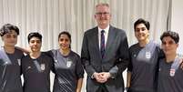 O ministro do Interior da Austrália, Tony Burke, ao lado das cinco jogadoras iranianas que obtiveram asilo no país. À esquerda do ministro estão Fatemeh Pasandideh, Mona Hamoudi e Atefeh Ramezanizadeh. À direita estão Zahra Ghanbari e Zahra Sarbali.  Foto: © HANDOUT / AUSTRALIAN DEPARTMENT OF HOME AFFAIRS/AFP / RFI