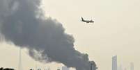 Avi&atilde;o da companhia a&eacute;rea Emirates voa perto de colunas de fuma&ccedil;a de um inc&ecirc;ndio perto do Aeroporto Internacional de Dubai, nos Emirados &Aacute;rabes Unidos, no dia 16 de mar&ccedil;o de 2026  Foto: AFP via Getty Images / BBC News Brasil