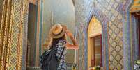 Mulher viajante usando vestido florido e chap&eacute;u no templo Wat Ratchabophit em Bangkok em um dia de ver&atilde;o  Foto: Getty Images / BBC News Brasil