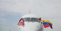 Pilotos do voo 3599 da American Airlines, partindo do Aeroporto Internacional de Miami com destino a Caracas, Venezuela, acenam com bandeiras venezuelanas e americanas antes da decolagem em um voo direto para a Venezuela, o primeiro entre os EUA e a Venezuela em sete anos, no Aeroporto Internacional de Miami, em Miami, Flórida, em 30 de abril de 2026.  Foto: AFP - CHANDAN KHANNA / RFI