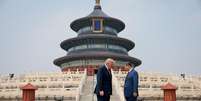 Os presidentes Trump e Xi estão em pé, frente a frente e com a cabeça levemente inclinada, diante de uma escadaria ornamentada que leva a um templo chinês decorado em tons de azul, verde, vermelho e dourado.
  Foto: Reuters / BBC News Brasil