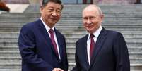 Xi Jinping e Vladimir Putin apertam as m&atilde;os em frente ao Pal&aacute;cio do Povo, em Pequim, a 20 de maio de 2026.  Foto: Alexander Kazakov/Pool Sputnik K - Alexander Kazakov / RFI