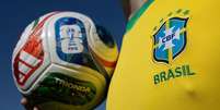 Pessoa com a camisa oficial da sele&ccedil;&atilde;o brasileira segurando a bola oficial da Copa do Mundo de 2026  Foto: Getty Images / BBC News Brasil