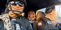 Dois policiais equatorianos com &oacute;culos de sol, capacetes e balaclavas, sentados em um carro com a jornalista da BBC Orla Guerin na parte de tr&aacute;s, vestindo uma jaqueta com a palavra 'IMPRENSA' em ingl&ecirc;s  Foto: Lee Durant/BBC / BBC News Brasil