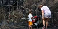 Uma m&atilde;e e seu filho inspecionam os arredores de sua casa em Le Porge, na segunda-feira, ap&oacute;s ela ter sido destru&iacute;da por um inc&ecirc;ndio florestal  Foto: Reuters / BBC News Brasil