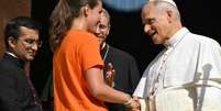 Uma jovem aperta a m&atilde;o do Papa Le&atilde;o XIV do lado de fora da catedral durante uma visita pastoral em Pavia, em 20 de junho de 2026.  Foto: AFP - MARCO BERTORELLO / RFI
